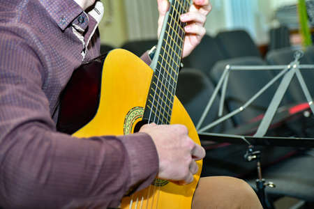 A young guitarist is rehearsing his part on the guitar in the middle of an empty concert hall.