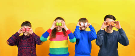 Three boys and a girl hold Easter eggs in front of them on a yellow background.の写真素材