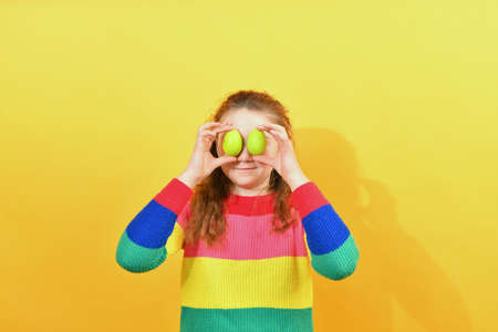 A boy in a colored sweater holds Easter eggs in front of him on a yellow background.の写真素材