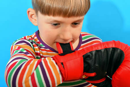 A young boxer puts gloves on his hands and helps to fasten them with his teeth, preparing a young athlete for a fight.の写真素材