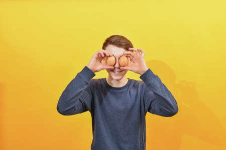 A boy in a gray sweater holds Easter eggs in front of him on a yellow background.の写真素材