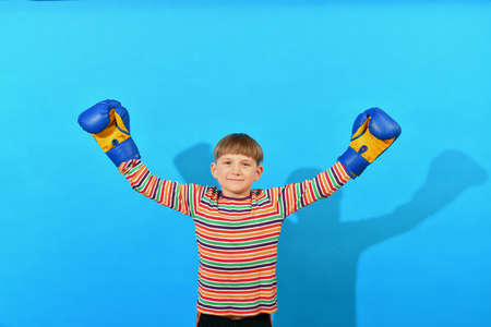 A joyful young boxer in blue gloves raised his hands up in a sign of victory over an opponent.の写真素材