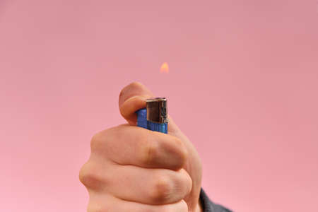 Burning lighter in the hand of a man on a pink background.の写真素材