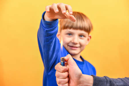 The boy holds his hand over the flame of a burning lighter.の写真素材