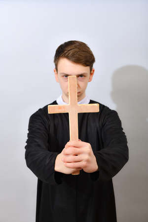 A young Catholic priest holds a cross in front of him. The concept of driving out the devil and evil...