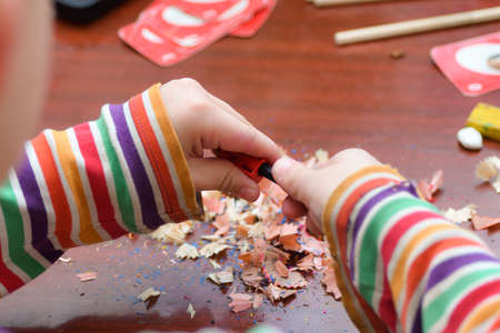 The child sharpens the pencil with a sharpener for further drawing with colored pencils.の写真素材
