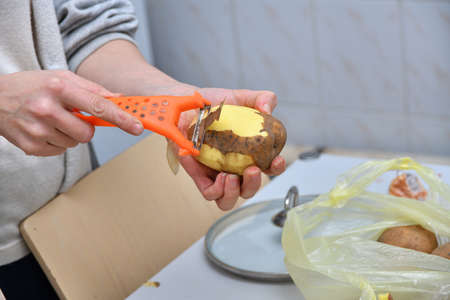 Hands of a young woman peeling potatoes with kitchen utensil on a wooden boardの写真素材