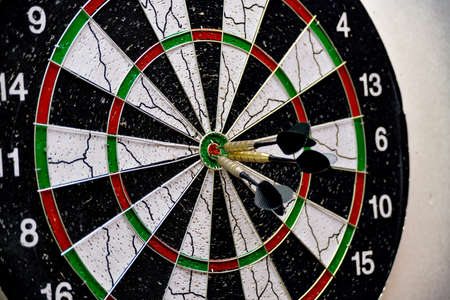 Three darts hit the center of the board while playing darts.