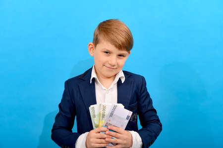 The boy holds in his hand bundles of euro banknotes of 100, 200 and 500 units. Rich child with money on a blue background.の写真素材