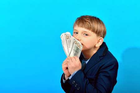 Boy in a suit sniffing dollar bills on a blue background. Greed for wealth concept.