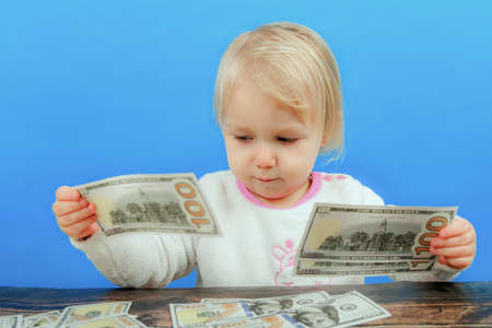A small child is sorting out dollars on the table and looking at them intently.の写真素材