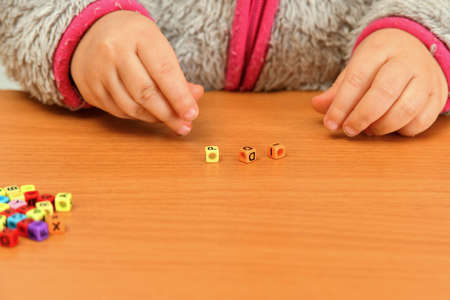A small child plays with colored letters and tries to put them into words. Preschool education...