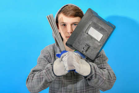 Young welder with electrodes and welding shield on a blue background.の写真素材