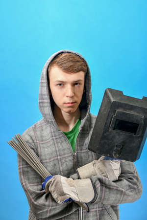 Young welder with electrodes and welding shield on a blue background.の写真素材