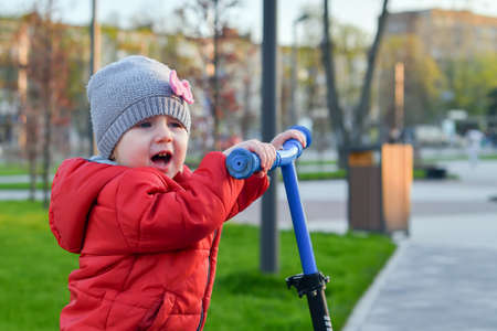 A little girl is riding a scooter on the sidewalk path in the park.の写真素材