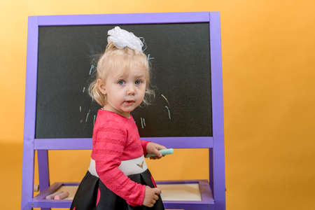 Little girl with colored chalk on the background of a children school board. The concept of preschool education for children.の写真素材