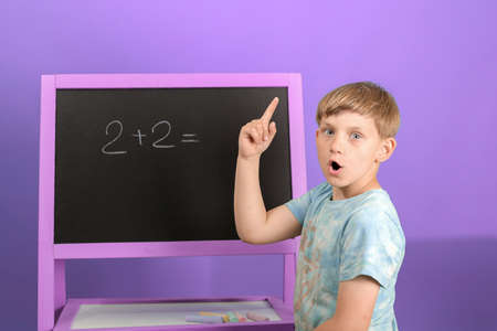 The boy solves the math equation 2 + 2 written on the blackboard. The child holds his finger up.の写真素材