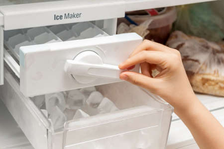 The girl pours ice cubes from the molds of the freezer to cool water and drinks.の写真素材