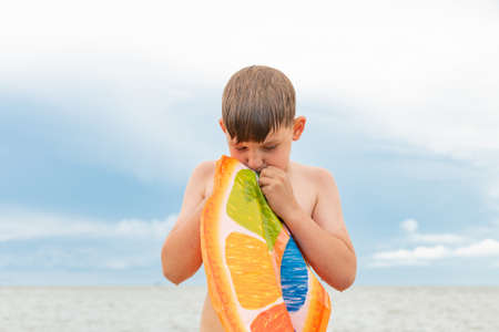 The boy inflates a swimming ring on the seashore.の写真素材