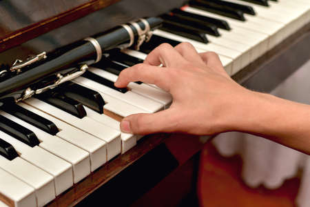 The clarinet lies on the black piano keys, the musician takes a chord on the white keys.