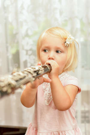 A little girl plays the clarinet. Teaching children music at a music school.の写真素材
