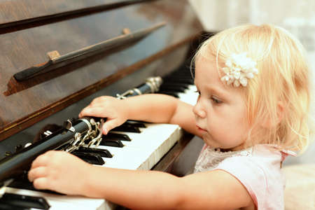 The little girl takes the clarinet lying on the black piano keys.の写真素材