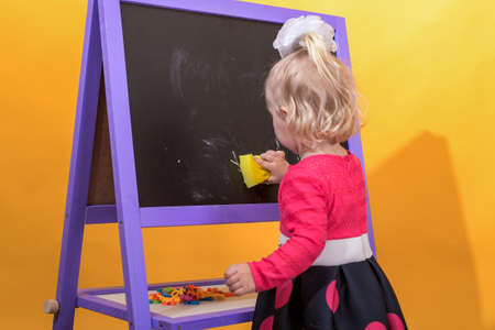 Little girl wipes the blackboard with a damp sponge. The concept of preschool education for children.の写真素材