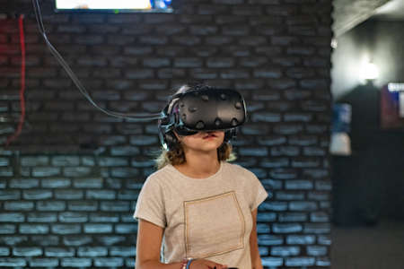 A girl in a computer club in a virtual reality helmet looks at content with VR glasses.