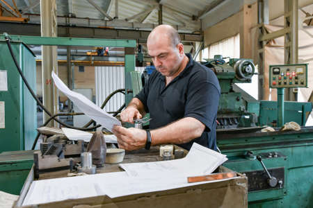 The worker measures the part with a vernier caliper and checks the size against the drawing.