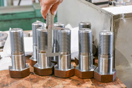 The worker measures the length of the thread on the bolt with a vernier caliper, after turning....