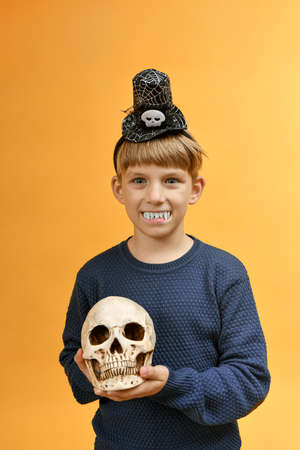 A boy with vampire teeth holds a skull in his hands. Halloween image.の写真素材