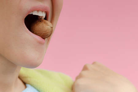 Girl holding walnuts with white teeth on a pink background.