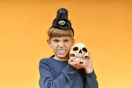 Angry boy with vampire teeth holds a skull in his hands. Halloween image.の写真素材