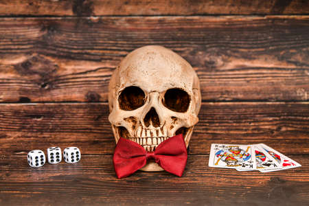 A skull with a bloody butterfly on a dark wooden background invites you to gamble for money.の写真素材