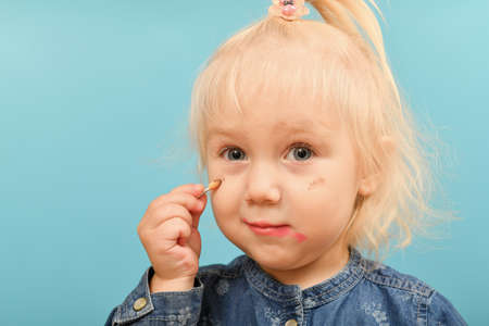 A little girl with painted lips puts shadows on her face.