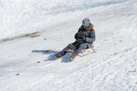 The guy goes down on a sled on a slippery snow slide.