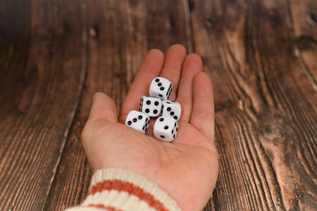 The man offers to play dice. White dice in a child's hand on a wooden texture.