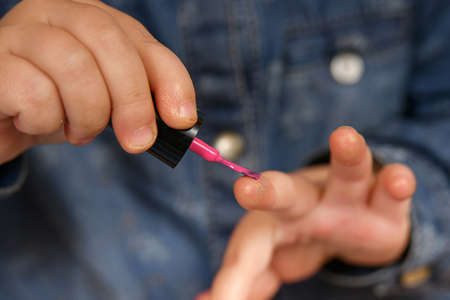 The little girl took the makeup from her mother and paints her nails with red varnish.