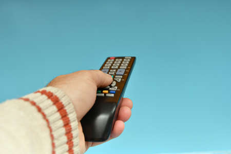 Tv remote control in the hand of a man on a blue background.