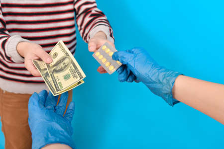 A doctor in blue medical gloves sells packaged pills to a patient for treatment for dollars. Profit...