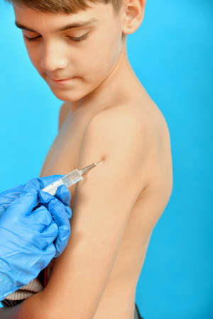 A doctor in protective medical gloves vaccinates a child. An injection of drugs into the shoulder of a teenager.の写真素材