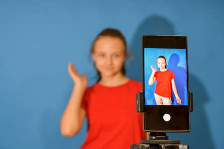 The girl grimaces and poses on a mobile camera in the studio to download and watch funny videos.