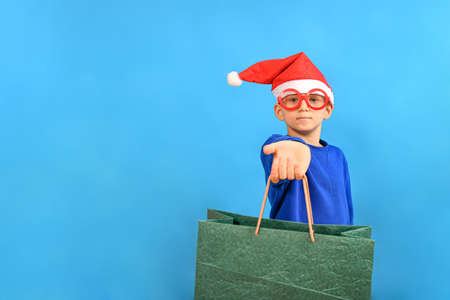 A boy in funny glasses and a Santa Claus hat holds out colored paper shopping bags. Shopping and shopping concept for Christmas and New Year.の写真素材