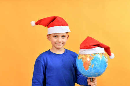 The santa claus hat is worn on the globe next to the child. Concept for worldwide celebration of New...