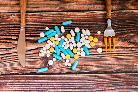 The pills are scattered on a wooden table, on the sides there is a knife and a fork for food.の写真素材
