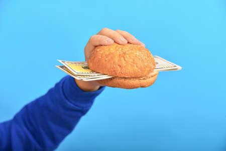 Burger with dollars in a man's hand on a blue background.