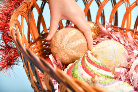 A girl arranges New Year's toys in a basket to decorate a Christmas tree.
