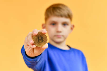 The boy holds a Bitcoin coin in his hand and offers to sell or buy it.の写真素材