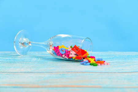 Colored wooden letters are scattered on a wooden table from a champagne glass.の写真素材