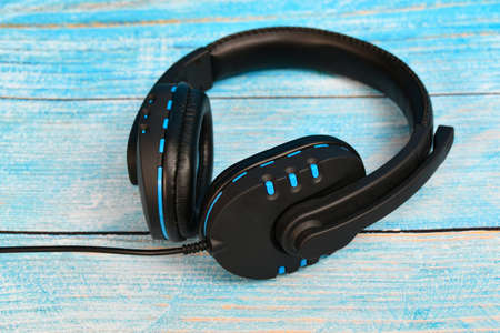 Black headphones with a microphone lie on a blue textured wood.